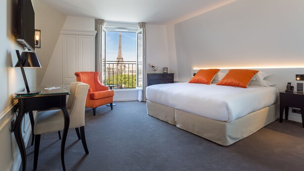 A hotel room with a bed, a desk, a chair, and a view of the Eiffel Tower. - Hôtel La Comtesse (Paris)