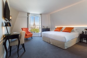 Habitación de hotel con cama, escritorio, silla y vistas de la Torre Eiffel.