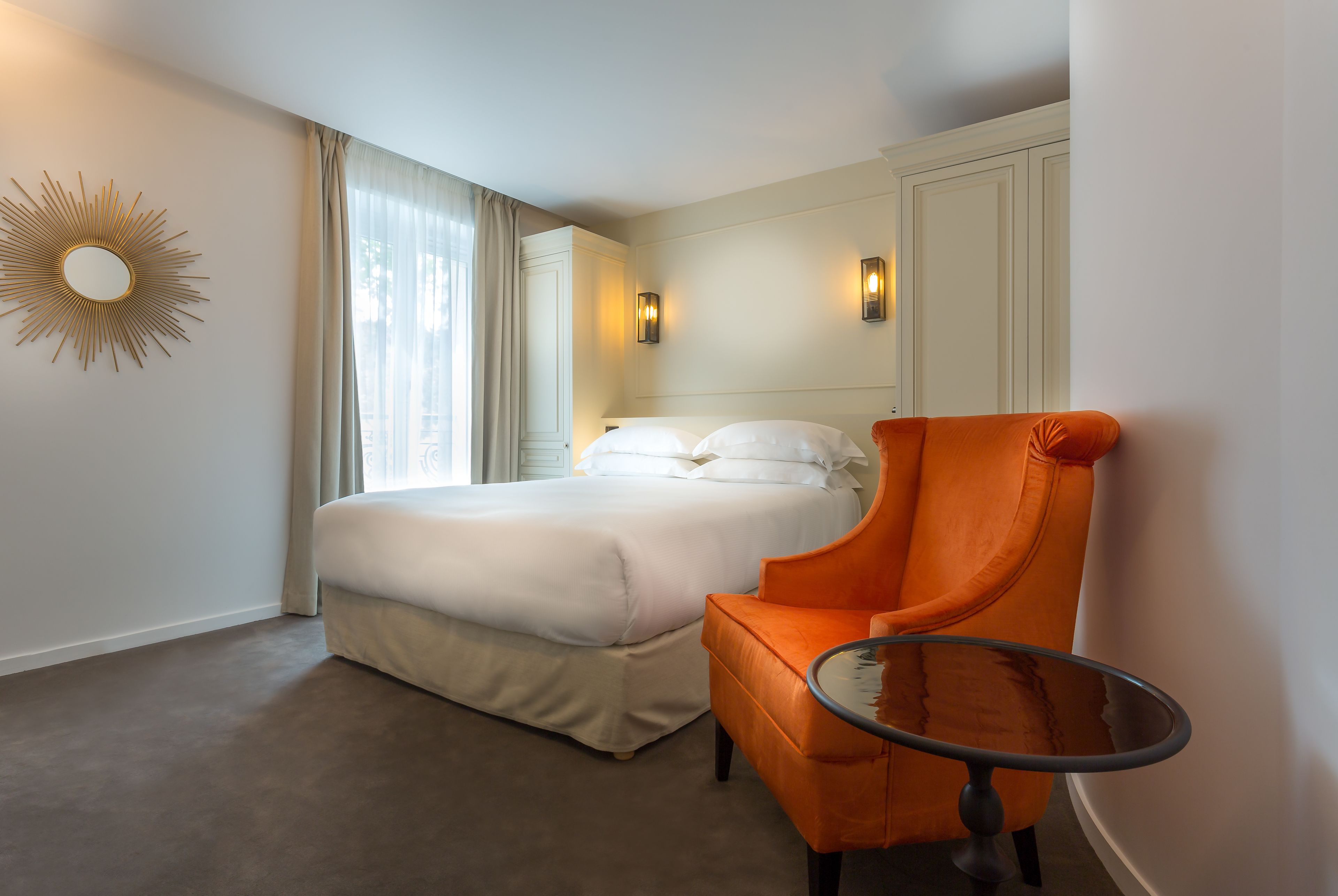 Una habitación de hotel con una cama, un sillón naranja, una mesita y un espejo colgado en la pared.