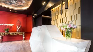 A modern reception area with a marble reception desk, a red wall with a decorative panel, and a ceiling with recessed lighting. - Hôtel La Comtesse (Paris)