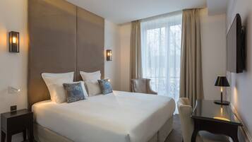 A hotel room with a large bed, a desk, a chair, and a TV.