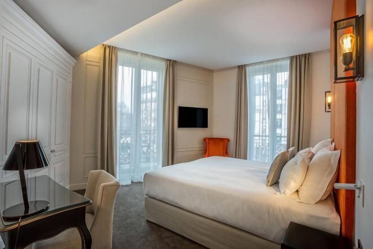 Une chambre d’hôtel avec un lit, un bureau, une chaise, une télévision et une fenêtre avec des rideaux.