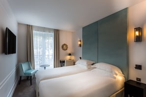 A hotel room with two beds, a desk, a chair, and a TV.