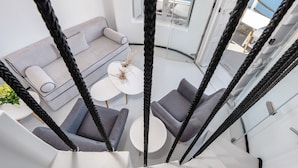 A modern interior with a grey sofa, two armchairs, and a small round table with decorative items. - Windmill Luxury Villa (Santorini)