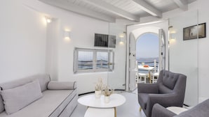 A modern living room with a sofa, armchairs, a coffee table, and a view of the sea through an open door. - Windmill Luxury Villa (Santorini)