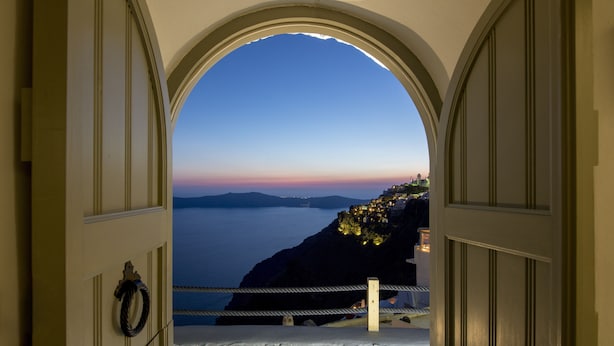 An arched doorway leading to a coastal view with a stone wall and a rope barrier. - Windmill Luxury Villa (Santorini)