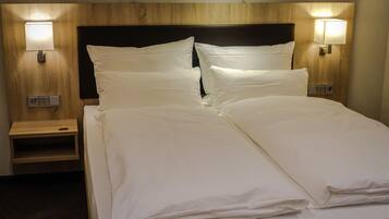 A neatly made bed with white linens, a wooden headboard, and two bedside lamps.