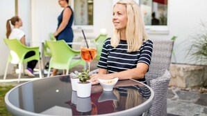 Een vrouw zit aan een buitentafel met een drankje en een plantje.
