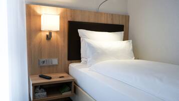Una habitación de hotel con una cama bien hecha, una lámpara de noche, una mesita de noche con un control remoto y un enchufe.
