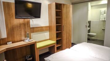 Ein Hotelzimmer mit einem Bett, einem Schreibtisch mit Stuhl, einem an der Wand montierten Fernseher und einem Holzschrank.