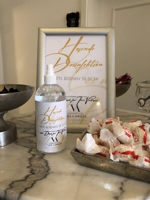 A bottle of hand sanitizer, a framed sign with text, and a tray of wrapped chocolates on a marble countertop. - VillaAdel Designroom (Alsfeld)