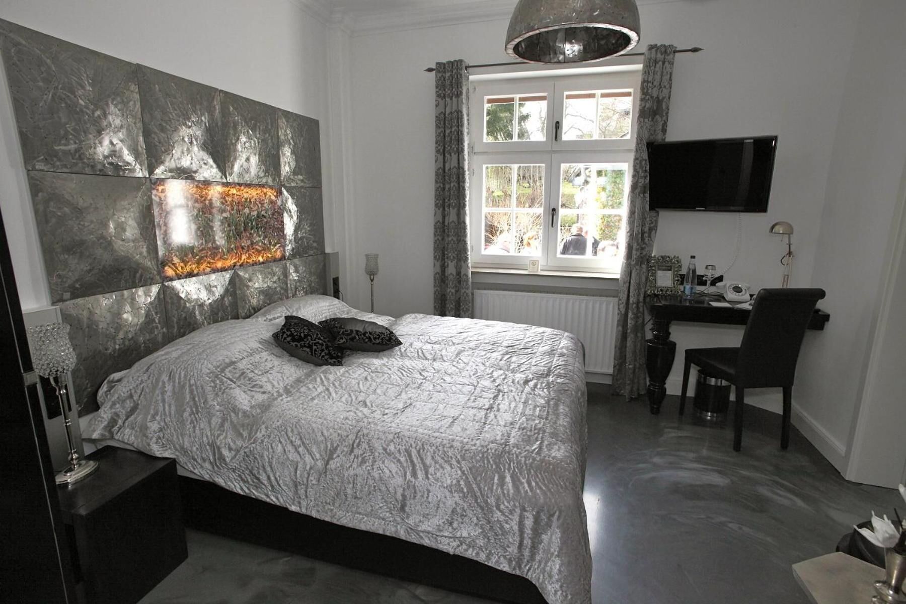 A bedroom with a bed, a desk, a chair, a TV, and a window with curtains.