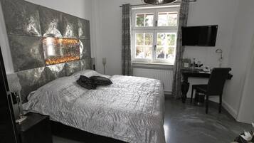 A bedroom with a bed, a desk, a chair, a TV, and a window with curtains.