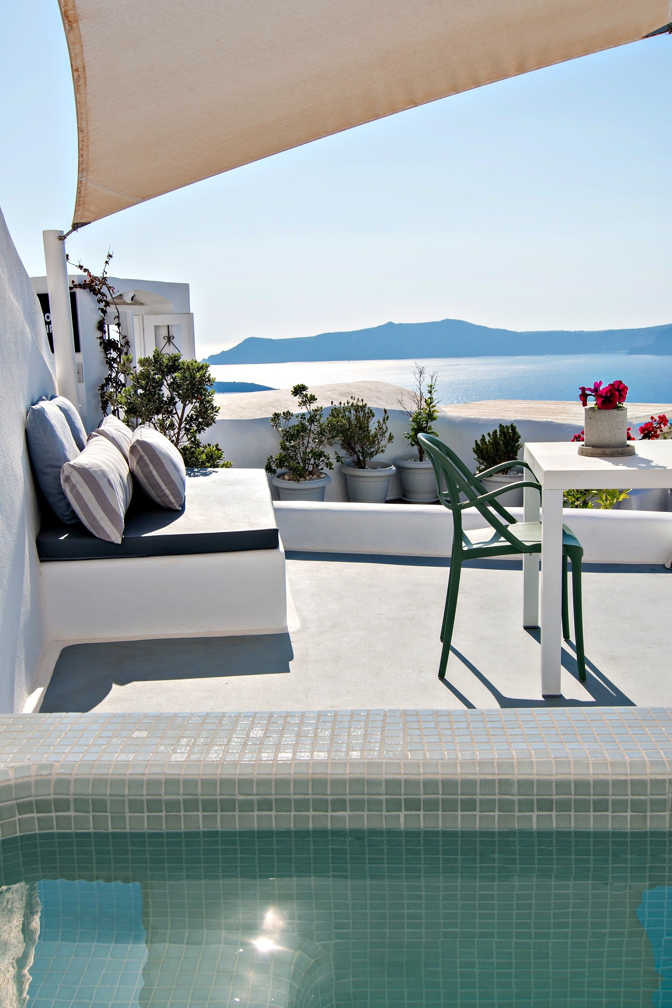A poolside area with a white outdoor seating area, a table with a vase of flowers, and a view of the sea.