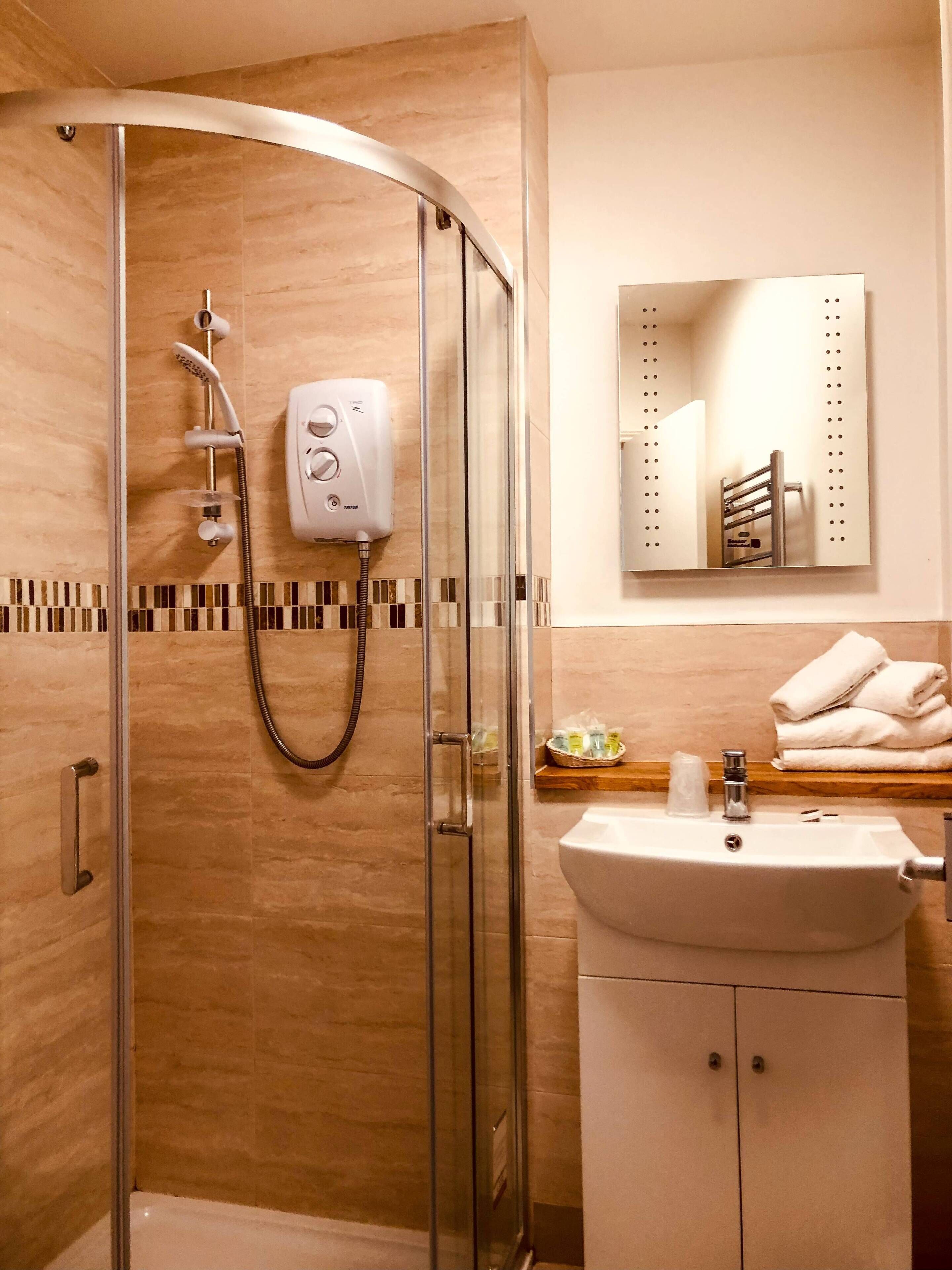 Un baño moderno con ducha envuelta en vidrio, un lavamanos blanco y un espejo sobre él.