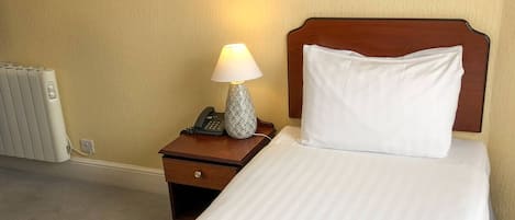 Una habitación de hotel con una cama individual, una lámpara de noche, un teléfono y un cuadro en la pared.