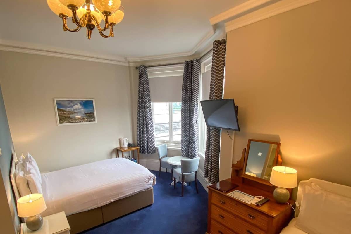 Quarto de hotel com duas camas, uma escrivaninha, uma cadeira, uma televisão e um candelabro.