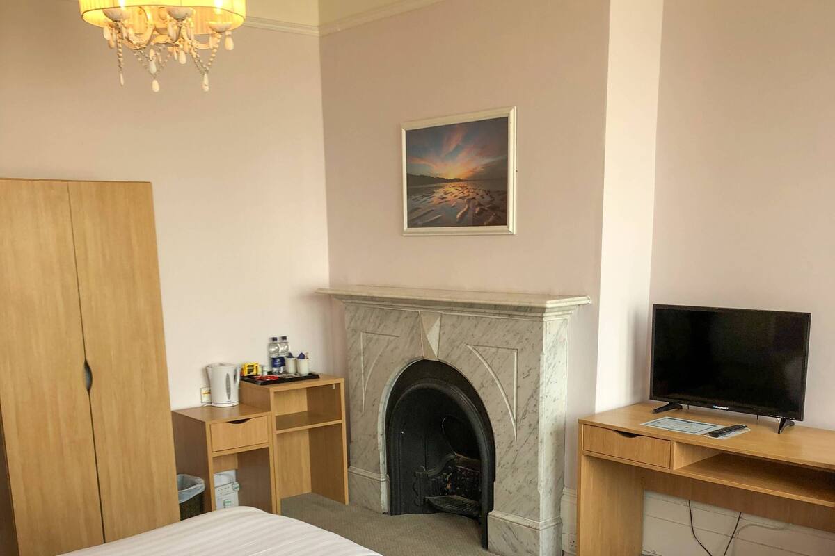 Quarto de hotel com duas camas, lareira, escrivaninha com televisão e um candelabro.