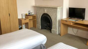 Habitación de hotel con dos camas, chimenea, escritorio con televisor y candelabro.