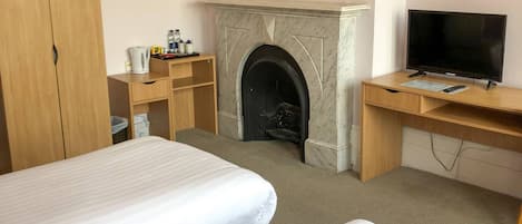 A hotel room with two beds, a fireplace, a desk with a television, and a chandelier.