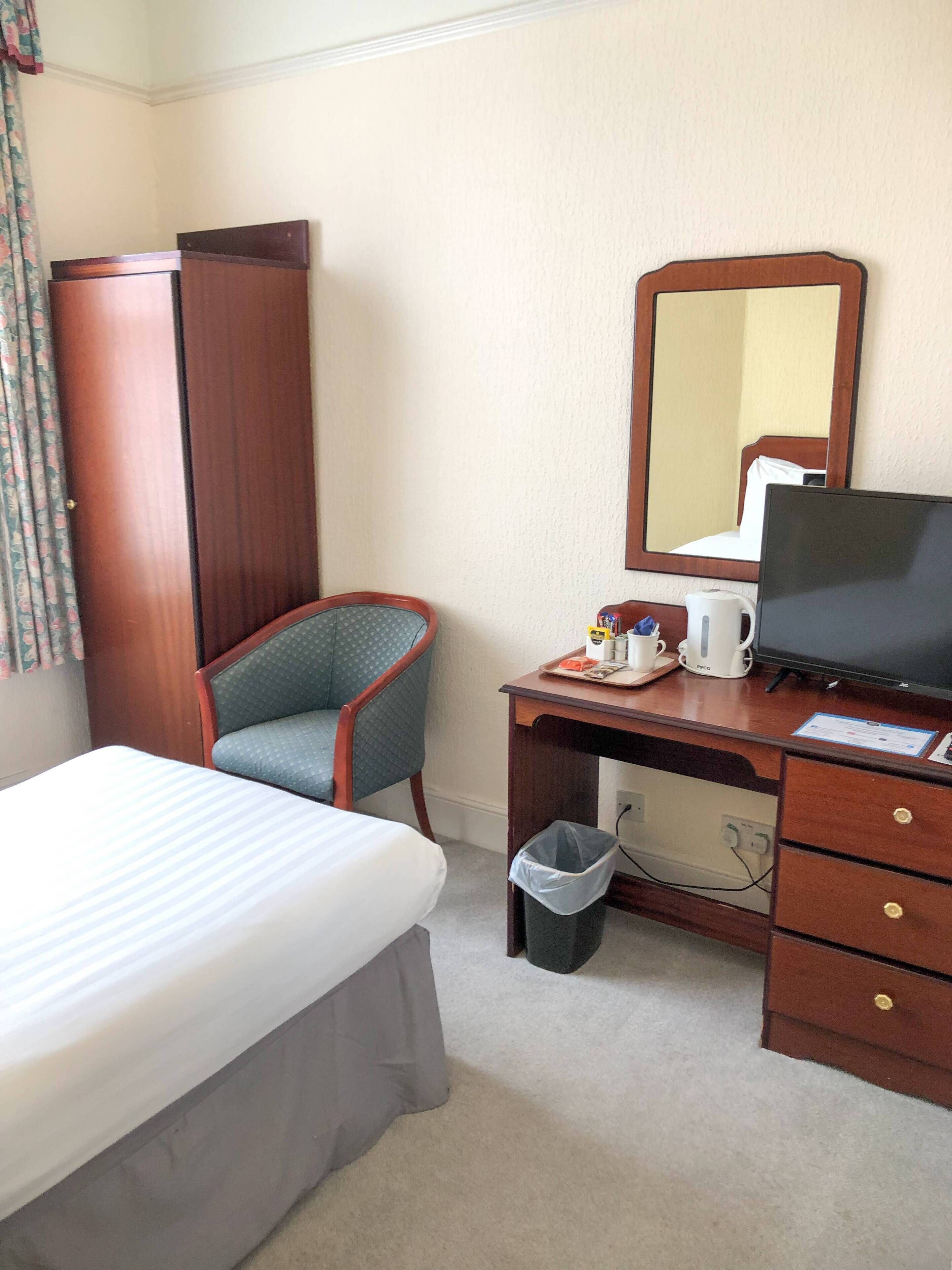 Een hotelkamer met een bed, een bureau met een computer, een stoel, een kast en een prullenbak.