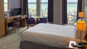 Habitación de hotel con cama, escritorio, silla, televisor y vista al mar.
