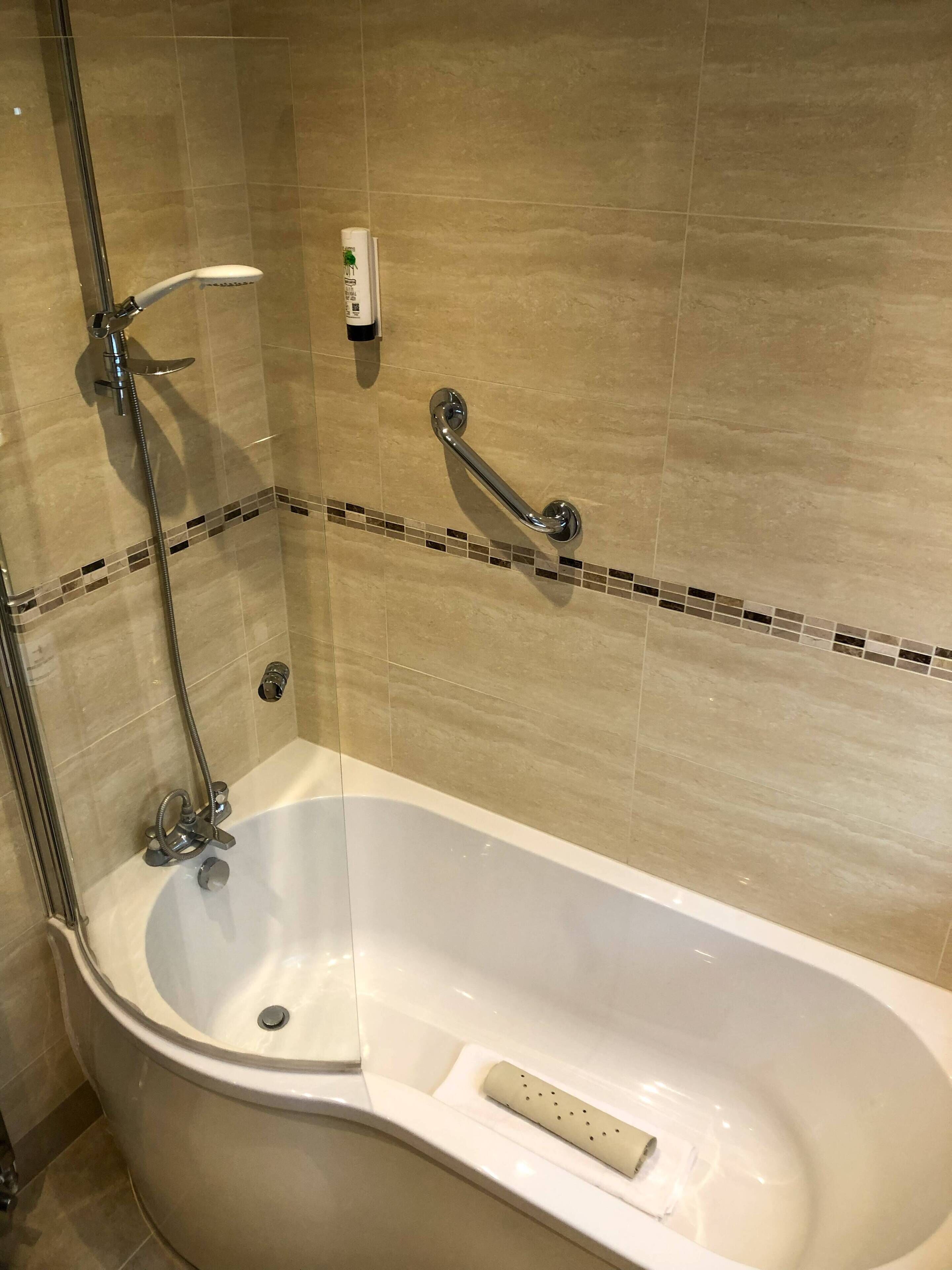 A modern bathroom with a freestanding bathtub, a handheld showerhead, and a grab bar.