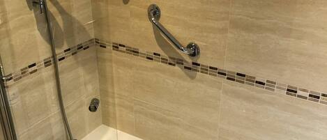 A modern bathroom with a freestanding bathtub, a handheld showerhead, and a grab bar.