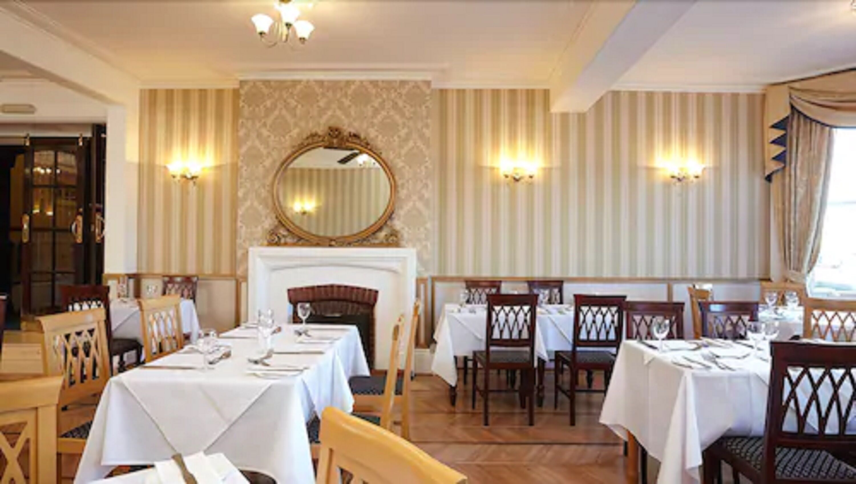 A formal dining room with multiple tables set for service, a fireplace, and decorative wall sconces.