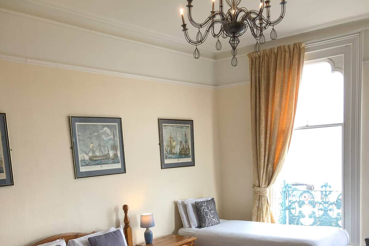 Quarto de hotel com duas camas, um candelabro, quadros nas paredes e uma janela com cortinas.