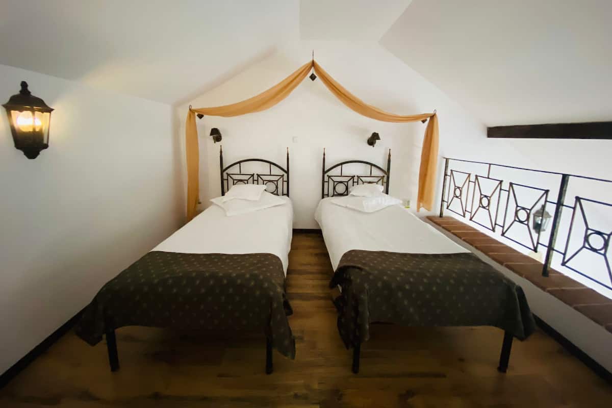 A room with two single beds, a wooden floor, a white ceiling, and a decorative wooden beam above the beds.