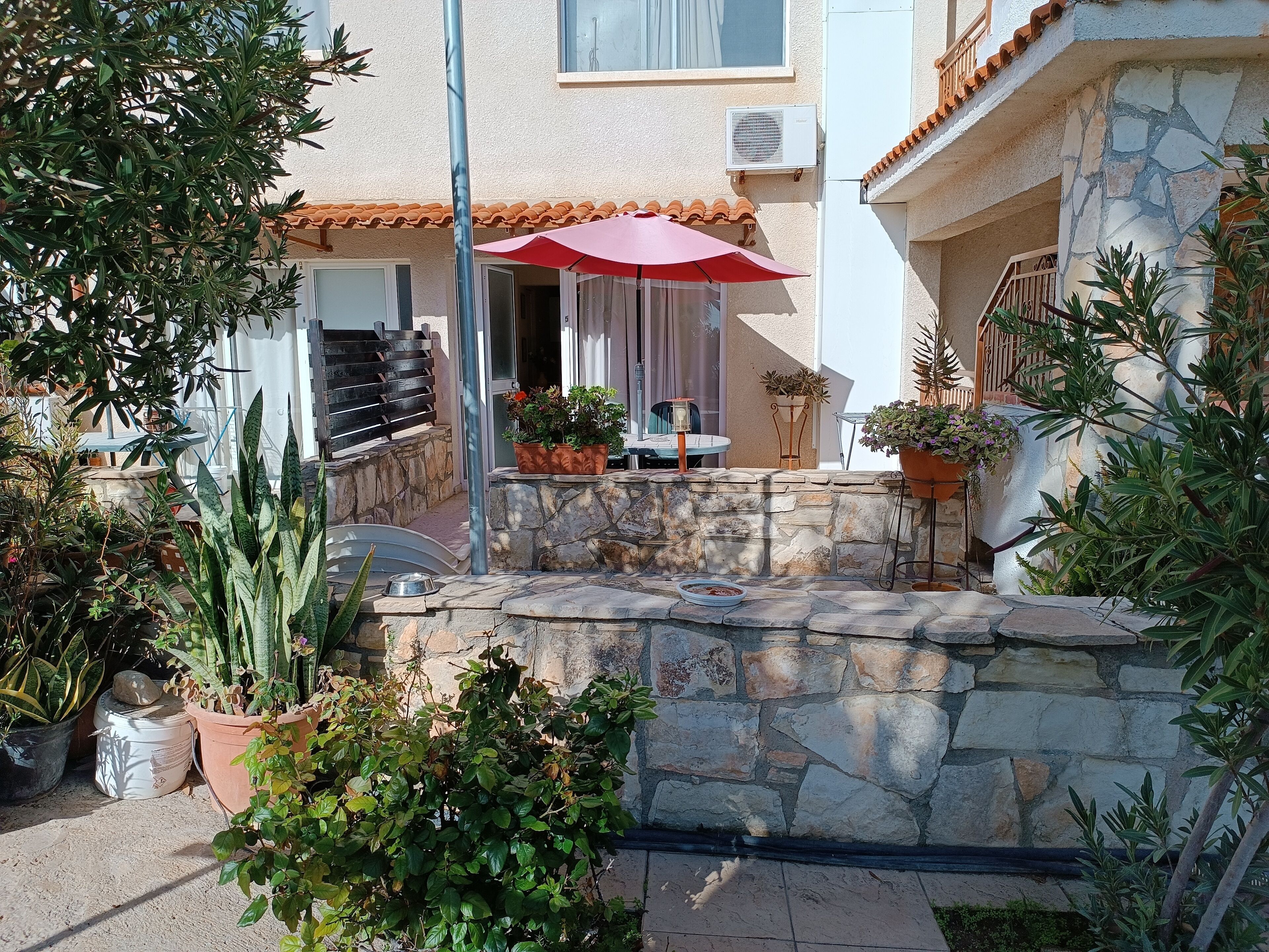 A stone wall with potted plants and a red umbrella.