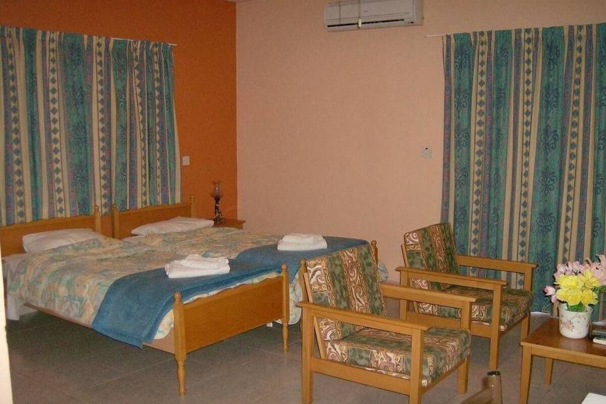 A hotel room with a bed, two chairs, a small table, and a vase with flowers.