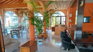 A spacious indoor area with wooden furniture, a central potted plant, and a kitchen area in the background. - Rantzo Holiday Apartments (Pissouri)