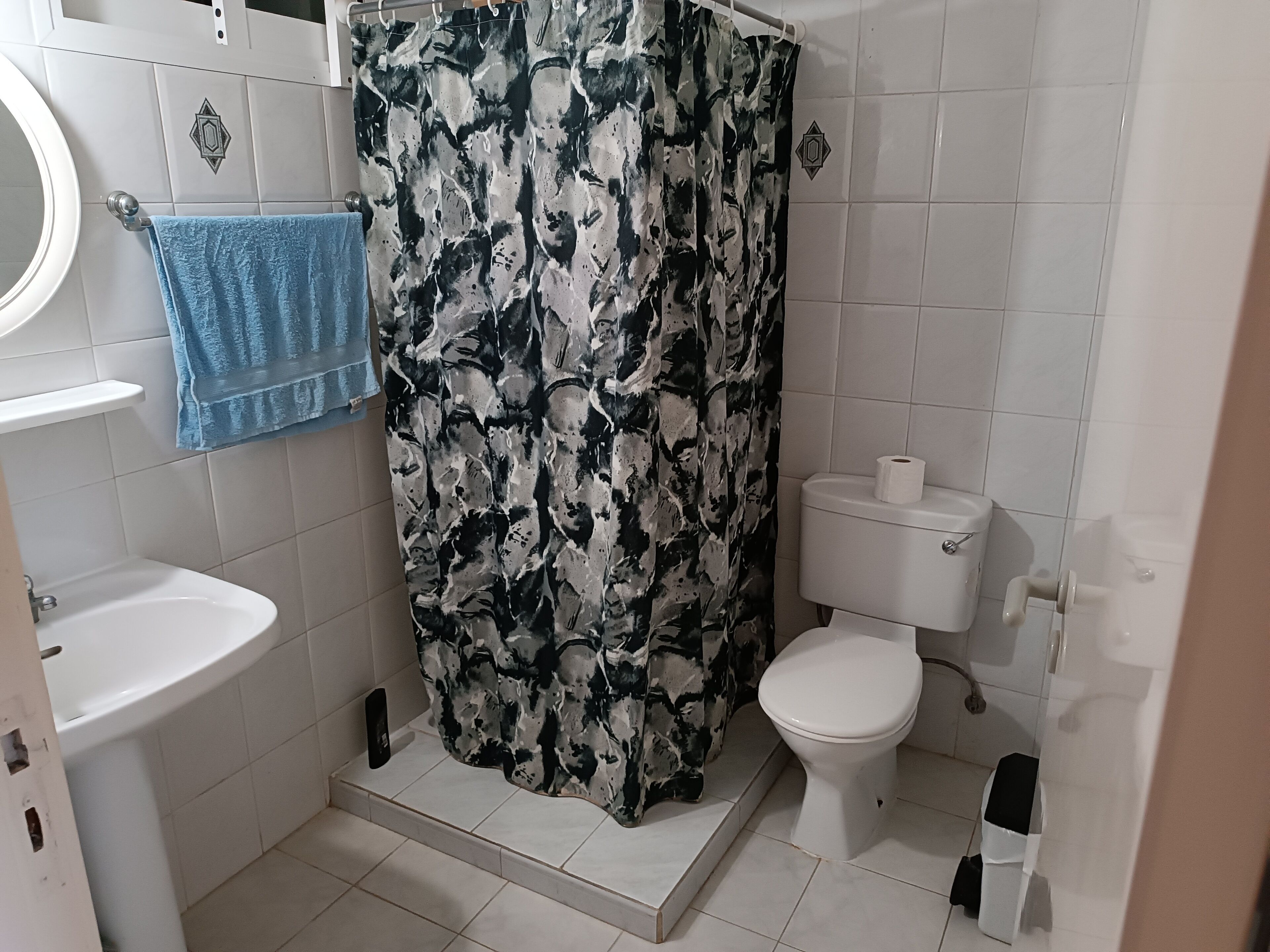 Un baño con lavamanos blanco, inodoro y cortina de ducha con estampado abstracto en blanco y negro.