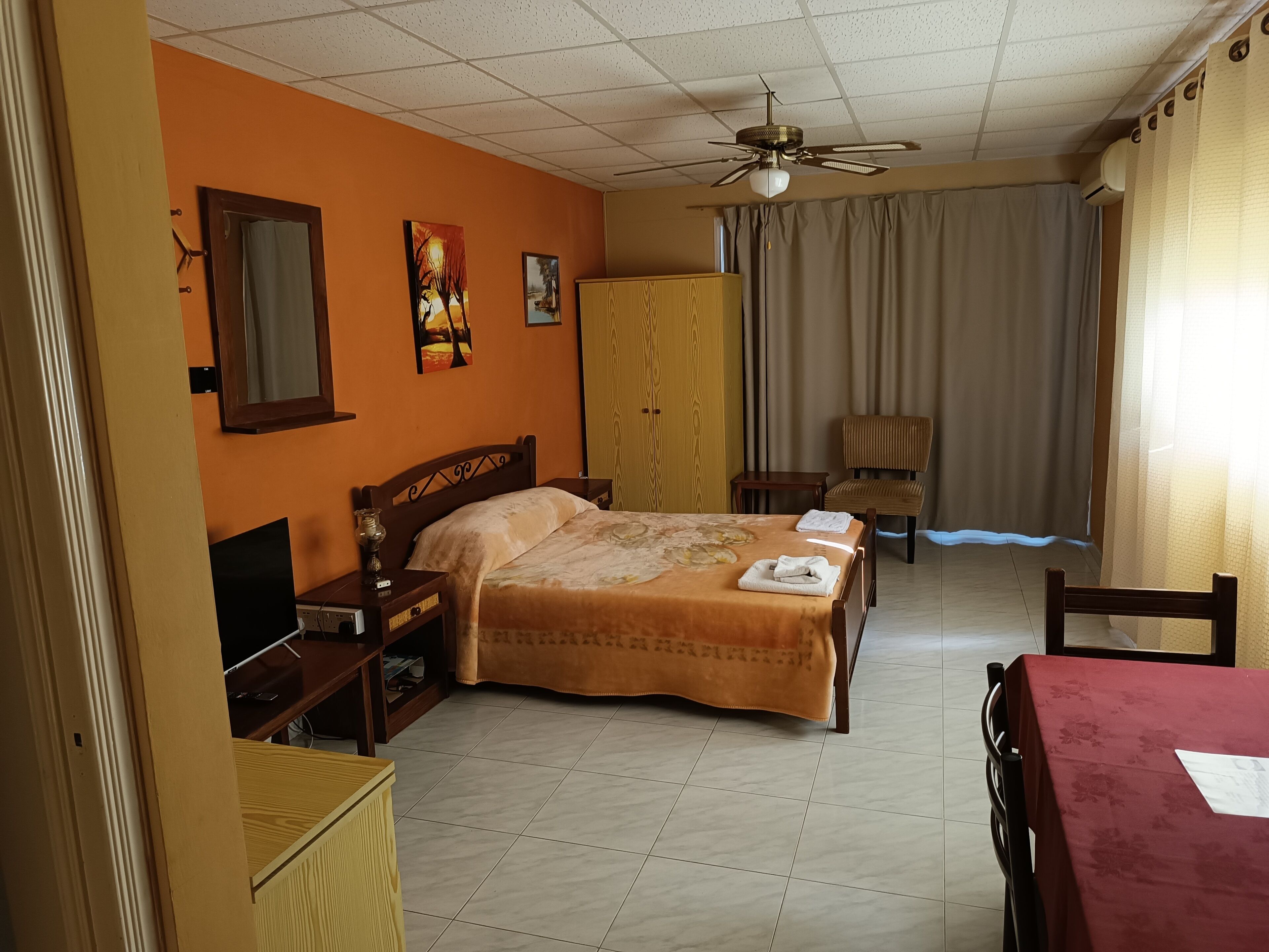 A hotel room with a bed, a desk, a chair, a wardrobe, and a ceiling fan.