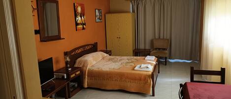 A hotel room with a bed, a desk, a chair, a wardrobe, and a ceiling fan.