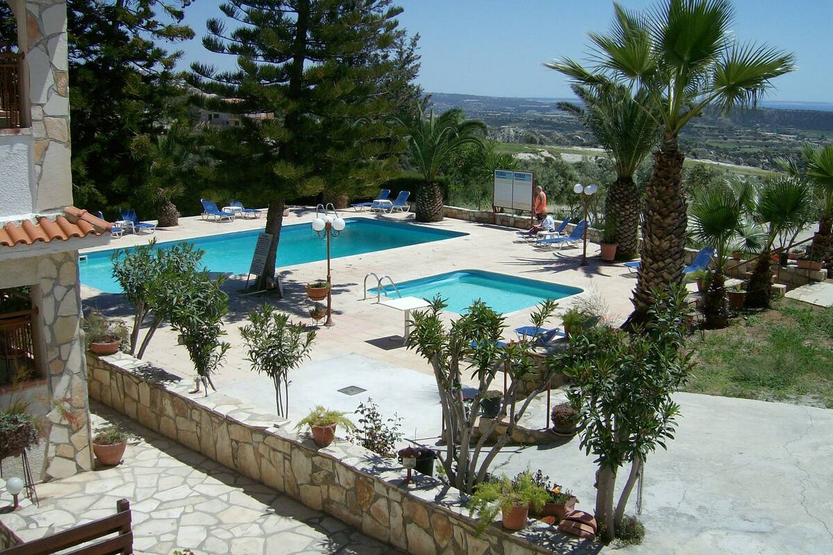 A pool area with a view of the landscape, surrounded by potted plants and lounge chairs.