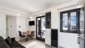 Una sala de estar moderna con sofá, mesa de comedor, sillas y una cocina con refrigerador y armarios.