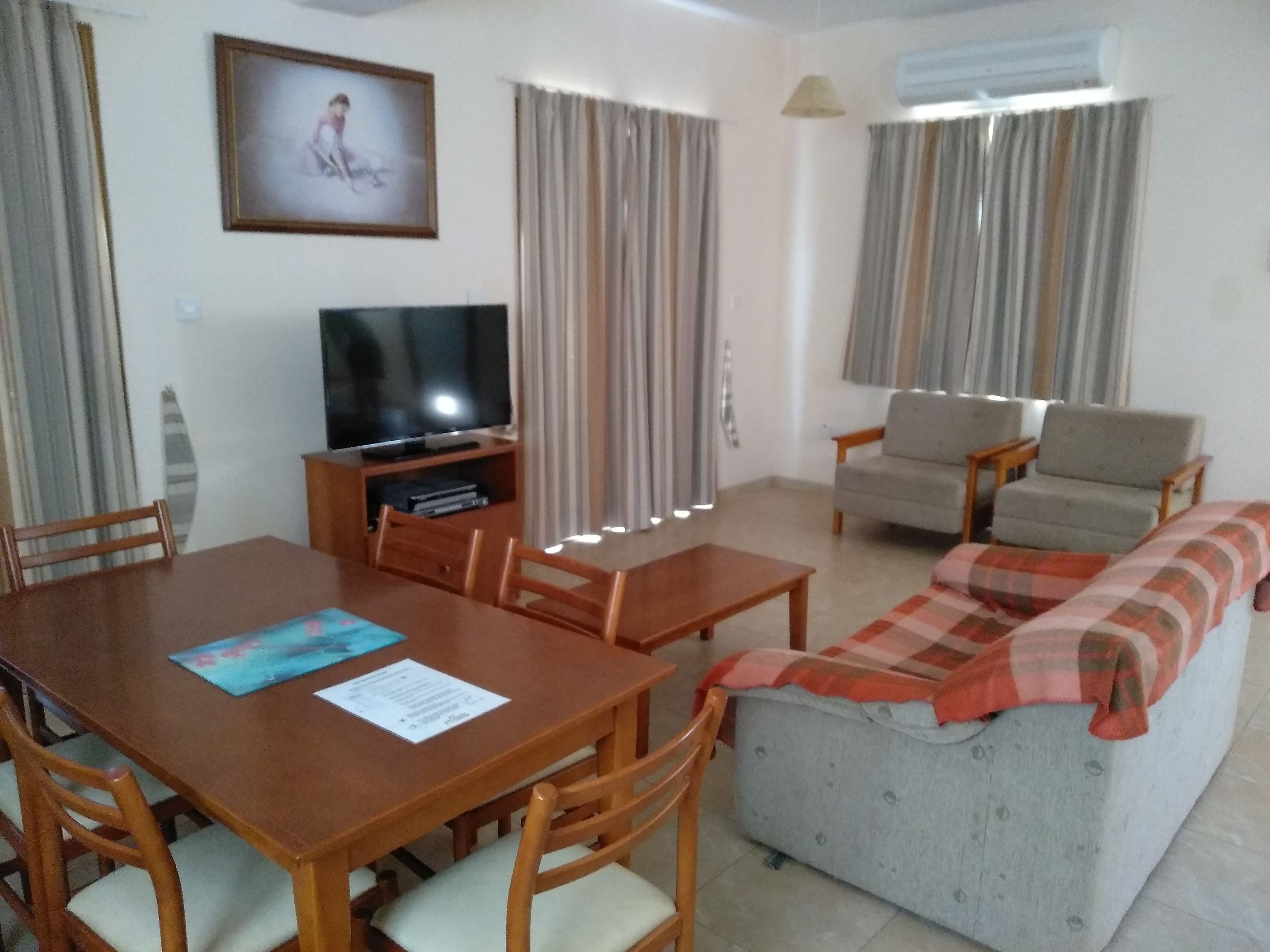 Ein Wohnzimmer mit Fernseher, Sofa und Esstisch.