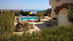 A pool area with a view of the sea, surrounded by greenery and a building. - Kapsalia Holiday Villas (Pissouri)