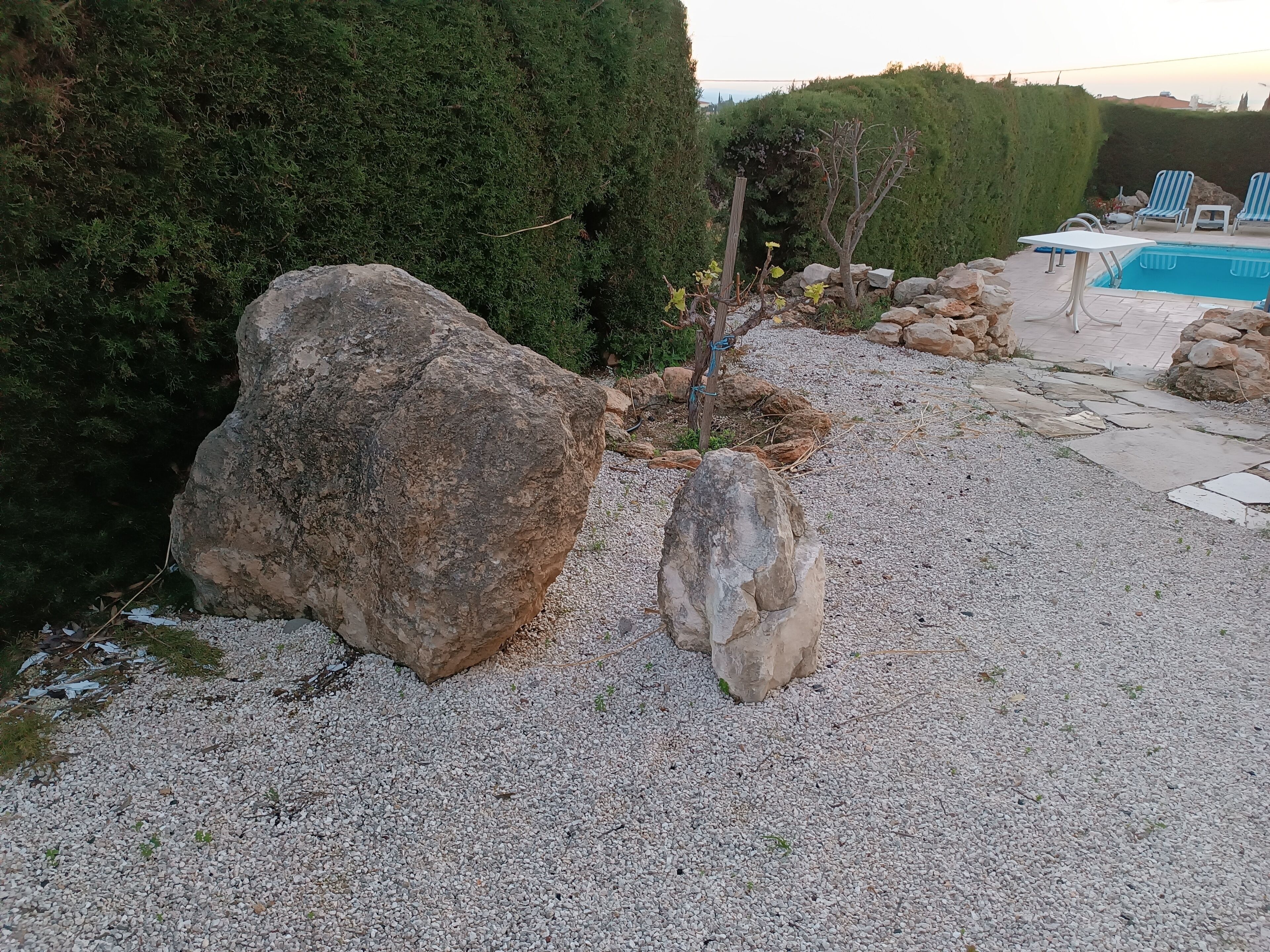 Un jardín con rocas grandes, una piscina y sillas de descanso.
