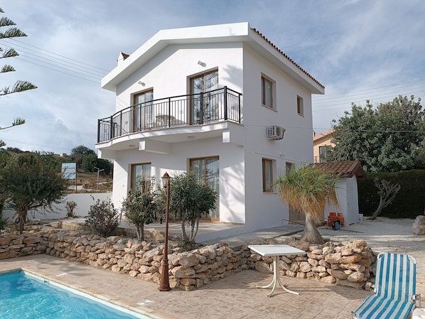 A two-story building with a balcony, a swimming pool, and a stone wall.