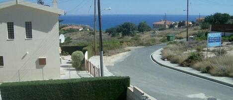 A coastal road with a pool area in the foreground, a building with a sign, and a view of the sea.