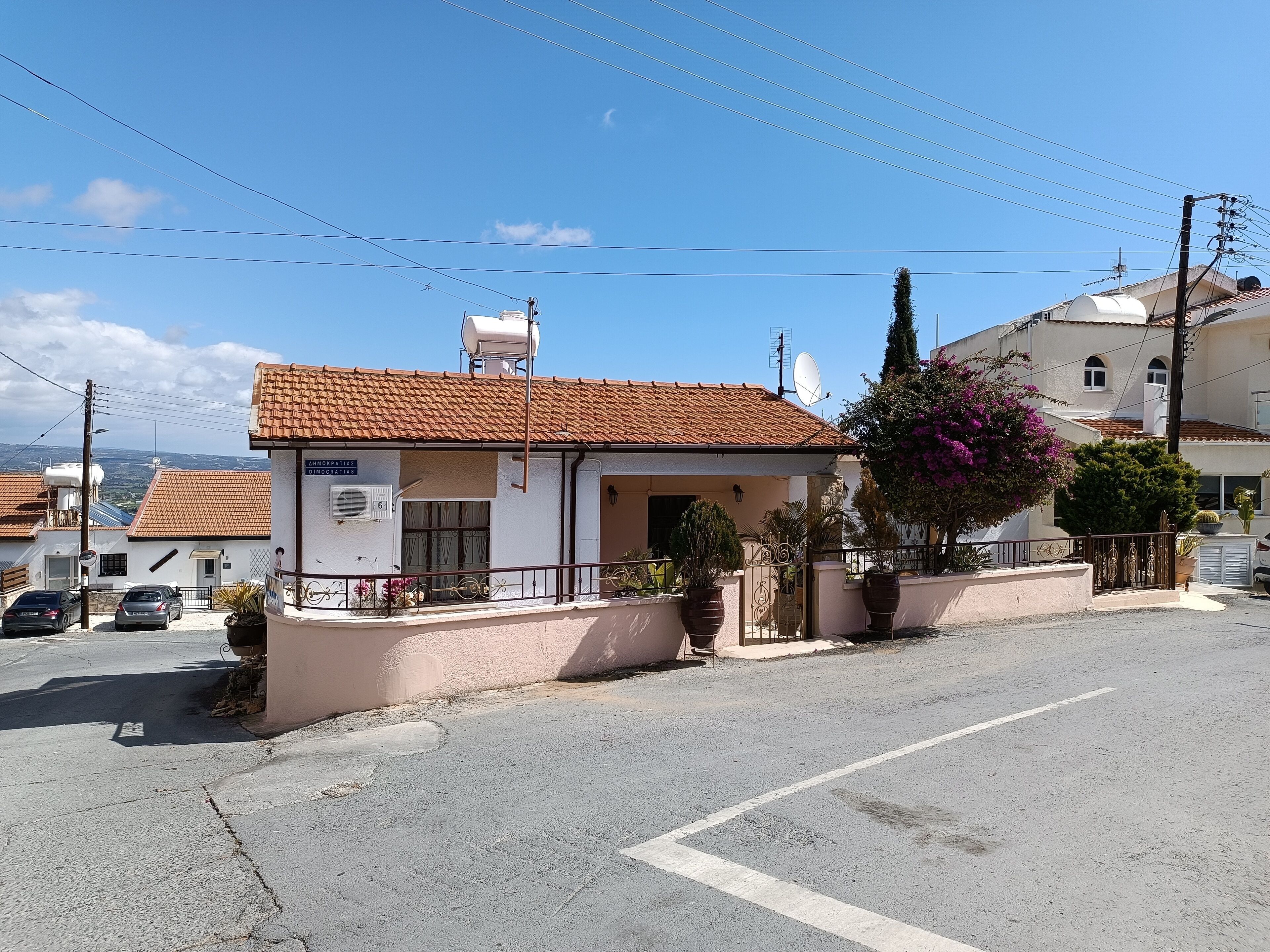 A small building with a tiled roof, a satellite dish, and a sign that reads "CHIMOKPATISIE DIOROTIKIAS."