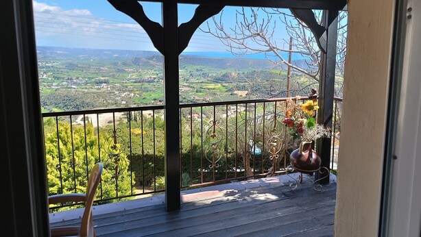 Un balcon donnant sur un paysage rural, une pergola en bois et une rambarde en métal agrémentée d’éléments décoratifs.