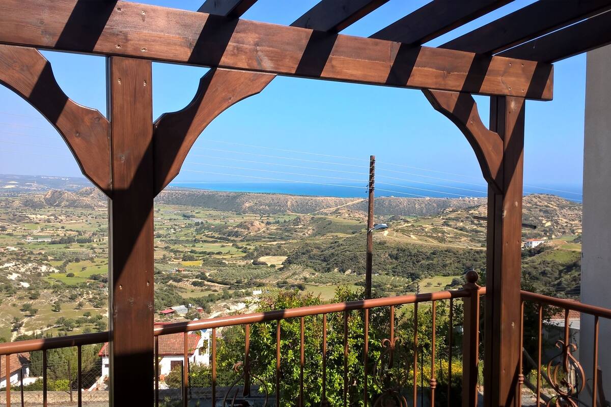 A balcony with a wooden pergola structure, overlooking a scenic landscape with fields and distant hills.