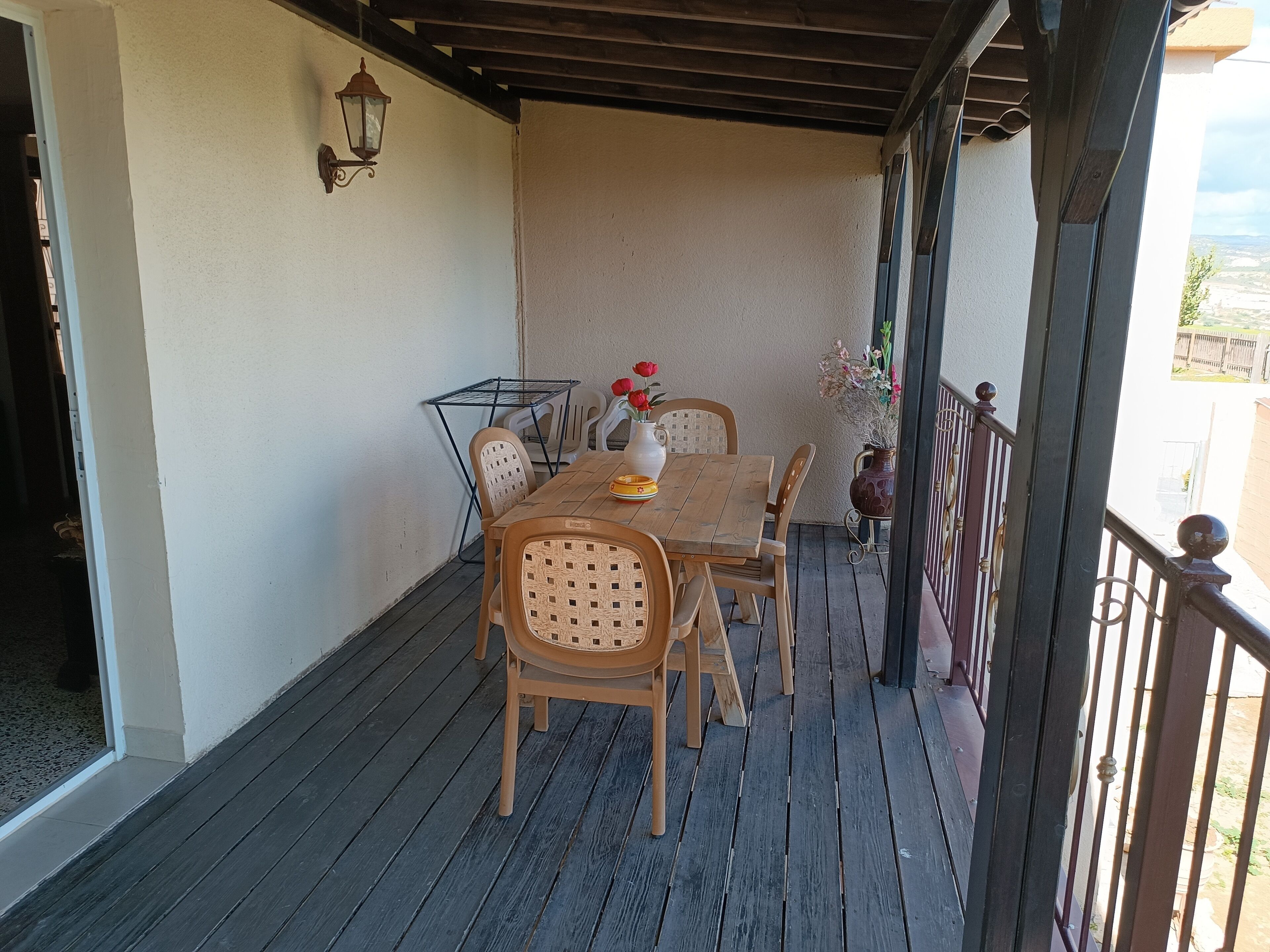 A wooden deck with a table and chairs, a hanging lantern, and a view of the outdoors.