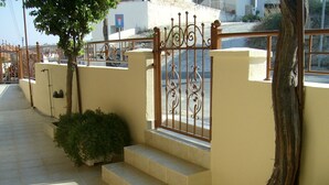 Un escalier menant à une entrée fermée par un portail en fer forgé décoratif, avec un arbre et un petit arbuste.