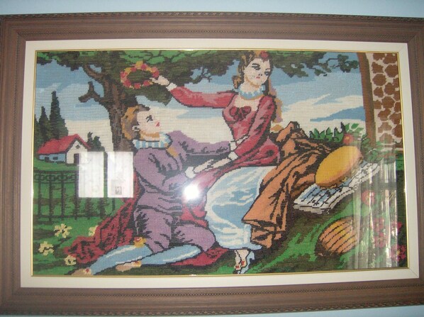 A framed cross-stitch artwork depicting a woman and a horse in a rural setting. - Patriko Village Home (Pissouri)